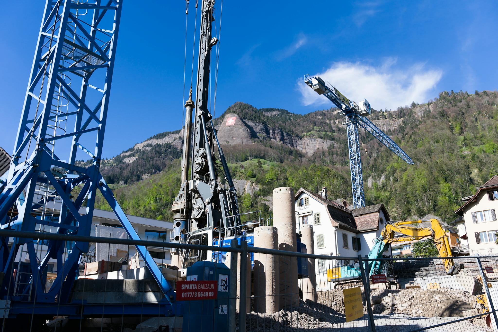 A bustling construction site with cranes against the picturesque Swiss Alps backdrop.