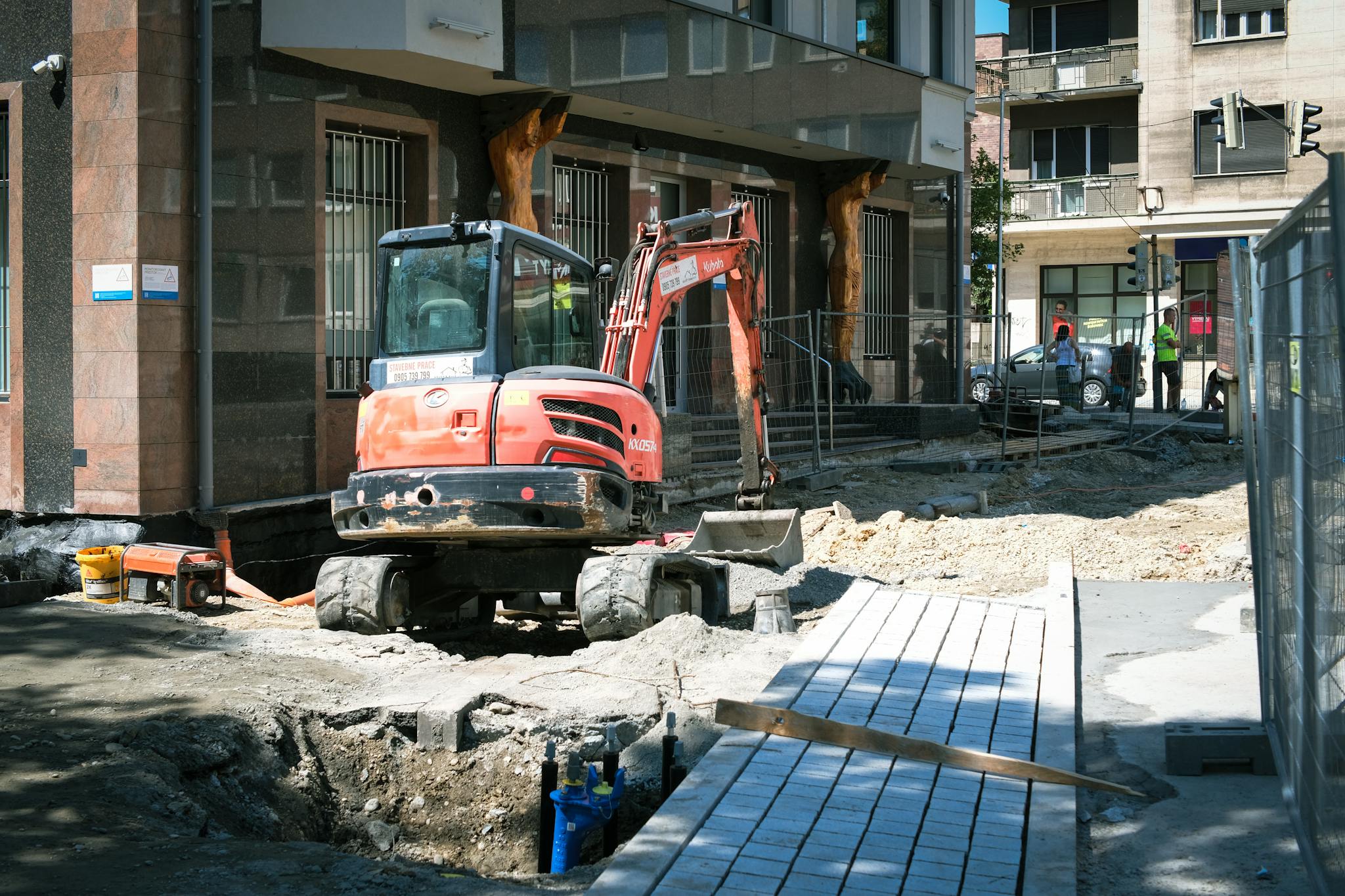 Street construction site in Bratislava with excavator and building.